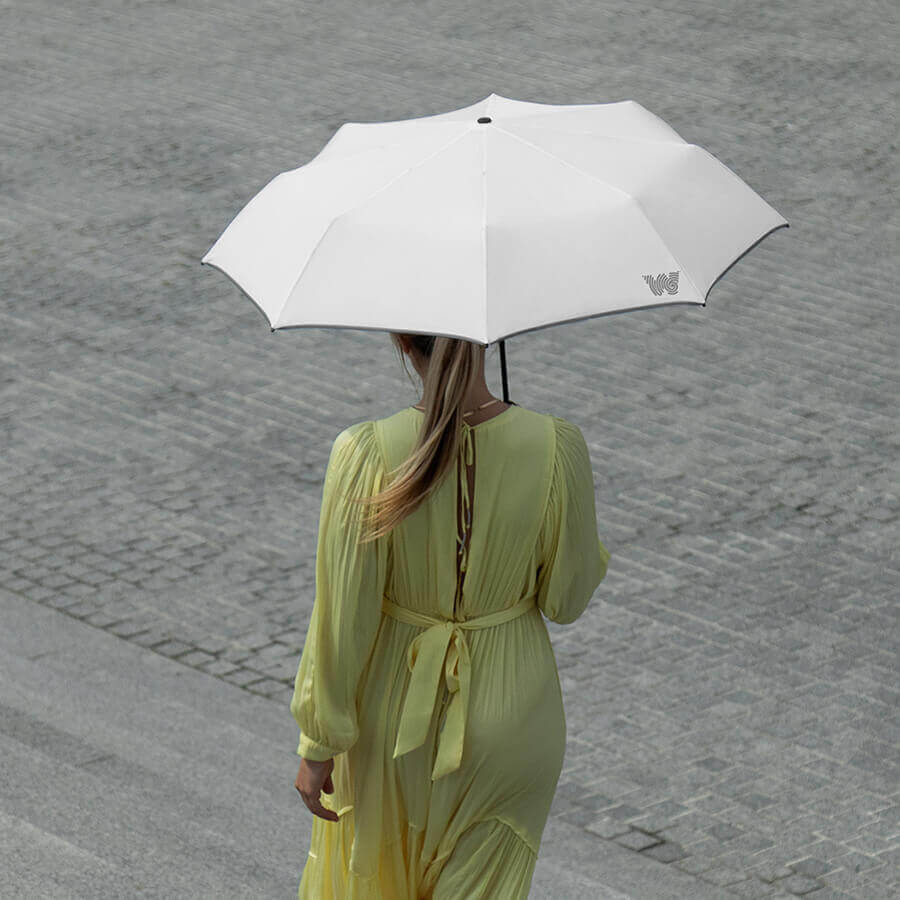 Woman walking down stairs while holding an opened Weatherman Travel Umbrella in white.