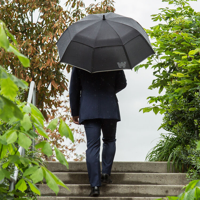 Man walking upstairs with Weatherman Stick Umbrella in black.