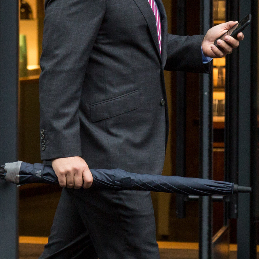 Man walking with closed Weatherman Stick Umbrella in navy blue.